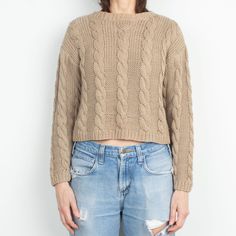 a woman standing in front of a white wall wearing ripped jeans and a brown sweater