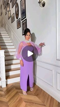 a woman in a purple dress standing next to a stair case with pictures on the wall