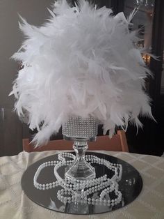 a table topped with a glass vase filled with white feathers