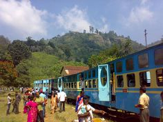 many people are standing near a blue and yellow train