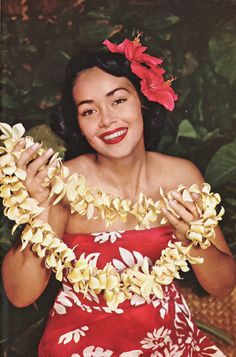 a woman in a red and white dress with flowers around her neck, smiling at the camera