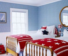 two beds in a room with blue wallpaper and white bedding, one has a red blanket on it