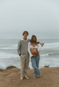 a pregnant woman standing next to a man on the beach