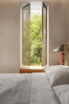 a bed with white sheets and pillows in front of a window that looks out onto the trees outside