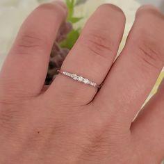 a woman's hand with a wedding ring on it and flowers in the background