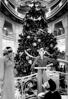 an old black and white photo of two women standing in front of a christmas tree