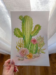 a person holding up a watercolor painting of a cactus and succulents