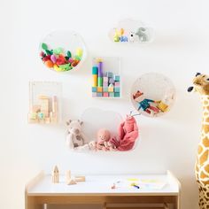 a giraffe standing next to a wooden table with toys on the wall behind it