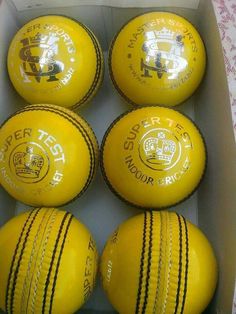 six yellow cricket balls in a box with white writing on the side and black stripes