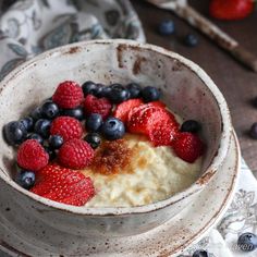 a bowl of oatmeal with berries and blueberries in it on a table