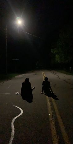 two people sitting on the side of a road at night