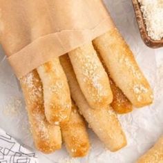 bread sticks with powdered sugar on them sitting in a paper bag next to two slices of bread