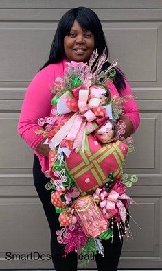 a woman holding a large pink and green christmas present in front of a garage door