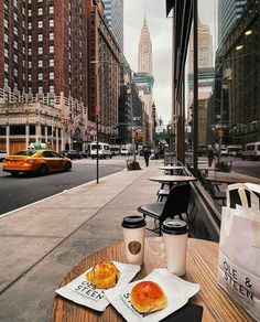 two pastries and coffee on a wooden table in front of a city street with taxi cabs