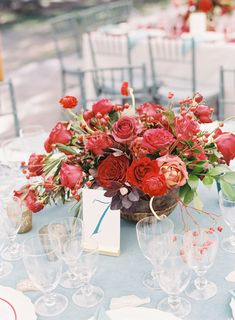 a vase filled with red flowers sitting on top of a table covered in wine glasses