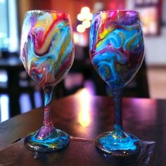 two colorful wine glasses sitting on top of a wooden table next to each other in front of a window