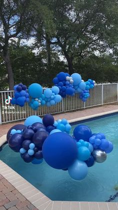 blue and white balloons floating in the air near a pool with a fence around it