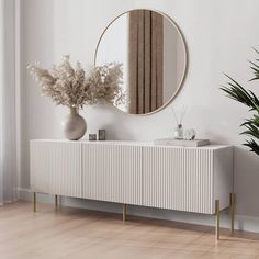 a white cabinet with a mirror and vase on it next to a potted plant