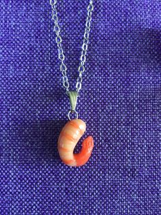 a necklace with an orange shell hanging from it's side on a purple cloth