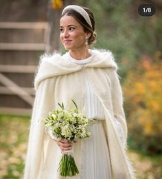 a woman in a white dress and fur coat holding a bouquet of flowers on her wedding day