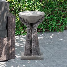 a concrete table sitting on top of a sidewalk next to a chair and shrubbery