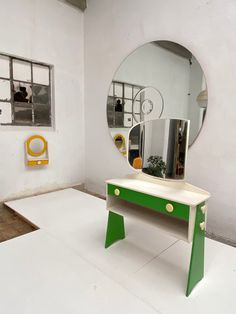 a green and white dresser sitting in front of a round mirror on top of a wall