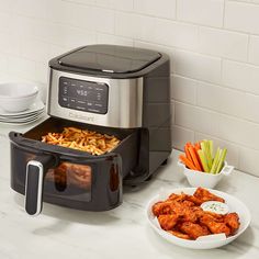 a black and silver air fryer with food in it on a counter next to plates