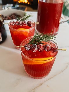 two glasses filled with red liquid and garnished with sprig of rosemary