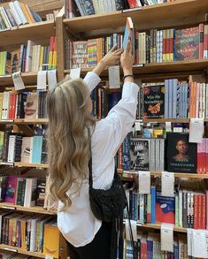 a woman standing in front of a bookshelf with her hands up to the ceiling