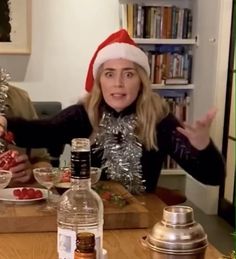 a woman wearing a santa hat sitting at a table in front of a bottle of booze