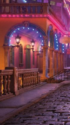 a woman is walking down the street in front of a building with lights on it