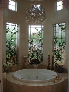 a bath tub sitting next to two windows with flowers on them in front of a chandelier