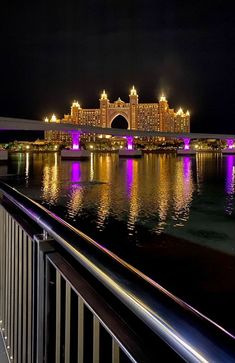 a bridge that is over some water with buildings in the background and lights on it