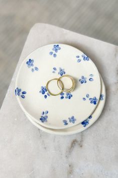 two gold wedding rings are placed on a blue and white floral ring dish that sits on a marble surface