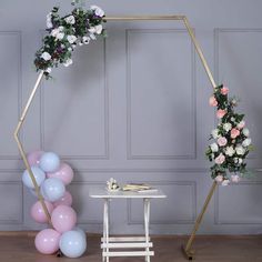 an arch with flowers and balloons in front of a small white table on the floor