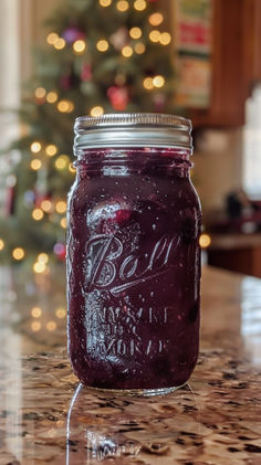 a glass jar filled with purple liquid sitting on top of a counter next to a christmas tree