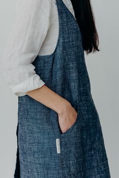 a woman wearing an apron with her hands in her pockets, looking down at the camera