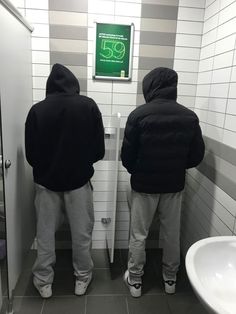 two men standing in front of a urinal with their backs turned to the camera