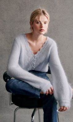 a woman sitting on top of a chair wearing jeans and a sweater over her shoulders