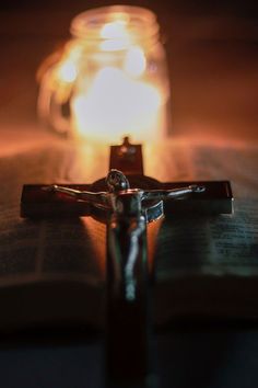 a cross sitting on top of an open book next to a lit candle in a jar