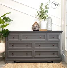 a gray dresser with two vases on top of it next to a potted plant