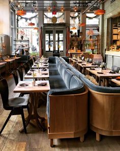 an empty restaurant with wooden tables and black leather chairs, along with lots of lights hanging from the ceiling