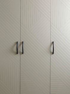 two black handles on the doors of a white cabinet with geometric pattern painted on it