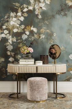 a table with a mirror, stool and flowers on it in front of a wall