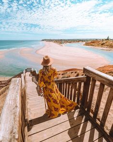 a woman in a yellow dress and hat is walking down the stairs to the beach