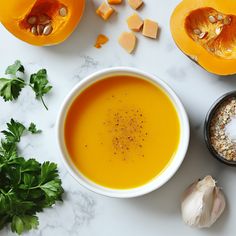 a bowl of carrot soup next to two halves of pumpkins and parmesan cheese