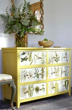 a yellow dresser sitting next to a chair and potted plant