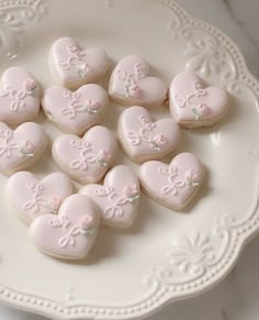 some heart shaped cookies are on a white plate with pink frosting and embellishments