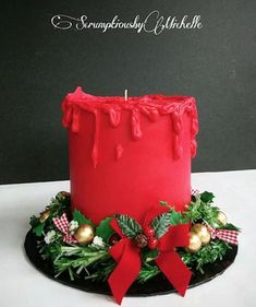 a red frosted christmas cake on a black plate with holly wreaths and baubles