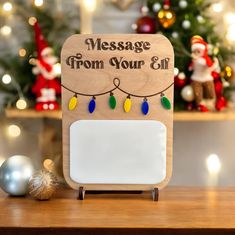 a wooden sign that says message from your elf with christmas lights on it and santa in the background